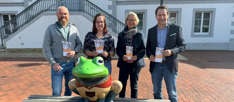 Vier Personen stehen hinter einer großen Froschfigur.
